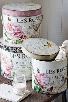 three buckets with roses painted on them sitting on a table next to a candle