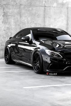 a black car parked in a parking lot next to a concrete wall and cement floor