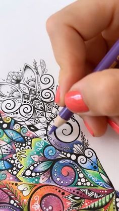 a woman's hand is holding a pencil and drawing an intricate design on paper