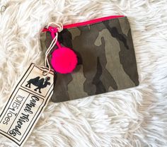 a pink pom - pom keychain is on top of a camouflage pouch