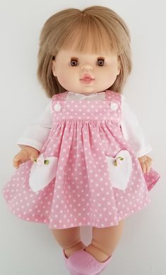 a doll with blonde hair wearing a pink polka dot dress and pink shoes, standing against a white background