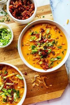 three bowls filled with soup on top of a wooden cutting board next to other dishes