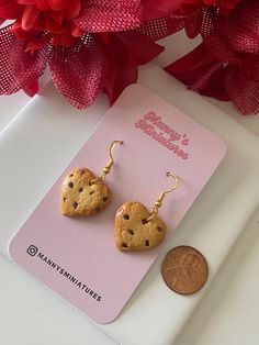 two heart shaped cookies hanging from earrings next to a penny