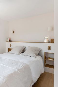 a white bed sitting in a bedroom next to a wooden shelf filled with pillows and blankets