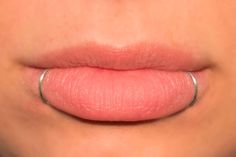 a woman's lips with pink lipstick on the bottom and silver ring around her lip