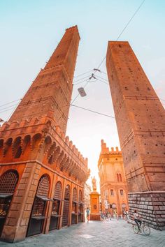 two tall brick towers with bicycles parked in front of them and people walking on the sidewalk