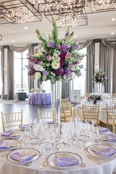 a tall vase filled with lots of purple and white flowers sitting on top of a table