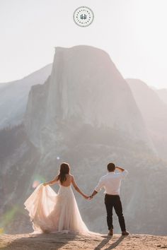 a bride and groom holding hands on top of a mountain