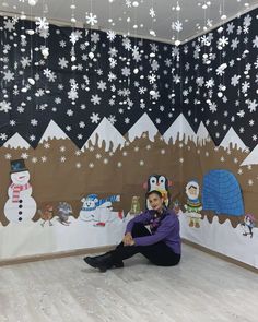 a woman sitting on the floor in front of a wall with snowflakes hanging from it