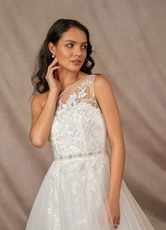 a woman in a white wedding dress posing for the camera with her hand on her cheek