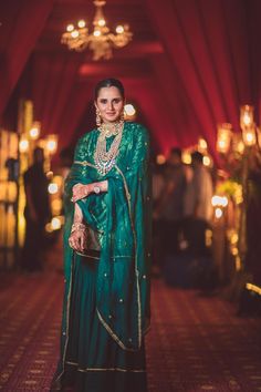 a woman in a green outfit standing on a red carpet with lights behind her and a chandelier hanging from the ceiling