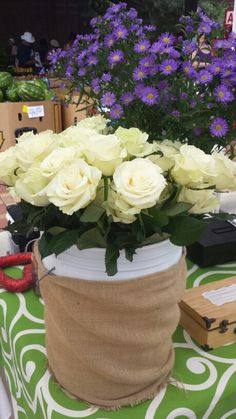 white roses are in a vase on a green tablecloth with purple flowers behind it