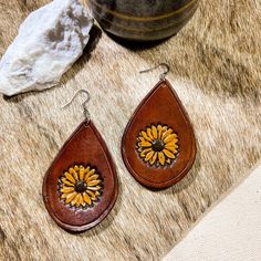 "Hand tooled earrings made from veg tanned leather and hand dyed in a rich brown shade with a yellow sunflower in the center. Lightweight and flexible for all day wear.  Dimensions: 2.5\"  Style: Teardrop  Care: No not keep wet for long periods of time, remove before swimming or showering. Store hanging or laying flat.  Nickel and lead free ear post for sensitive ears  Each item is uniquely handcrafted and might have slight variations  Follow us on Instagram! https://www.instagram.com/bovinebell Tooled Earrings, Sunflower Leather Earrings, Rustic Hand Tooled Leather Earrings, Artisan Brown Hand Tooled Earrings, Hand Tooled Teardrop Bohemian Earrings, Artisan Brown Teardrop Earrings, Tooled Sunflower, Rustic Brown Hand Tooled Earrings, Brown Shade