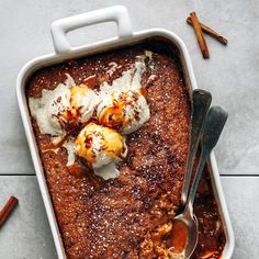 a casserole dish with cinnamon rolls and ice cream on top, next to two spoons