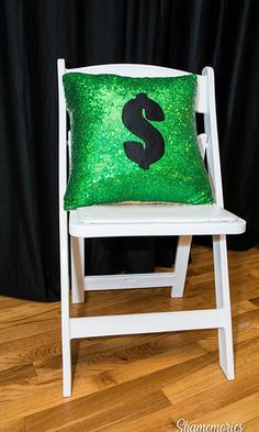 a white chair with a green sequin pillow sitting on it's back in front of a black backdrop