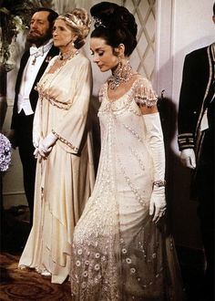 two women in white dresses and tiaras standing next to each other, one is wearing an elaborate headpiece