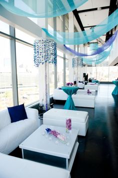 a room filled with white couches and tables covered in blue draping next to tall windows