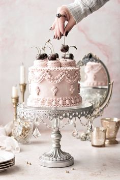 a person placing cherries on top of a pink frosted cake with icing