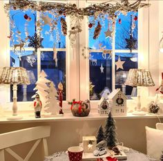 a table with christmas decorations on it in front of a window and lit up windows