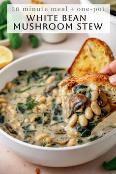 a hand holding a piece of bread over a bowl of white bean and spinach stew