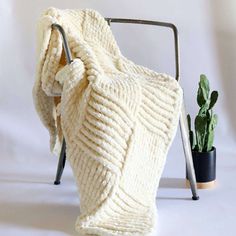 a white blanket sitting on top of a chair next to a potted plant