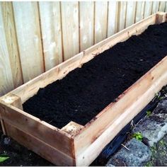 a wooden planter filled with dirt next to a fence