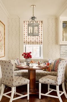 a dining room table with two chairs and a bench in front of a window that has red flowers on it