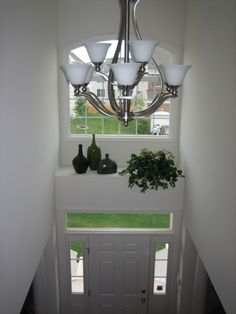 a chandelier hanging from the side of a window above a planter and vases