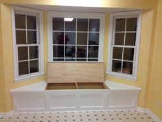 an empty room with two windows and a bench in the corner, all painted yellow