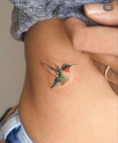 a small hummingbird tattoo on the side of a woman's stomach is shown