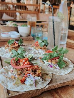 three tortillas with meat, tomatoes and lettuce on a wooden tray