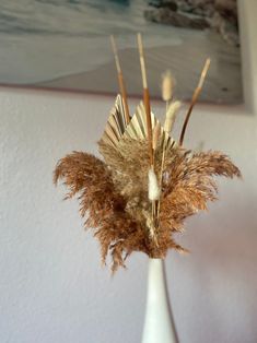 a white vase filled with dried plants on top of a table