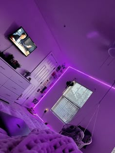 a bedroom with purple lighting and a tv on the wall above it, in front of a window