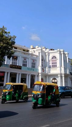 three green and yellow tuks driving down the street in front of a white building