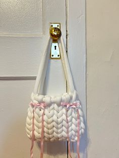 a white purse hanging on a door handle with pink ribbons and a golden ball in the center