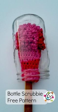 a glass jar filled with pink and red crocheted items sitting on top of a wooden stick