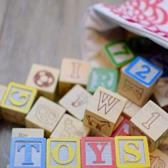 wooden toy blocks spelling the word toys on top of a wood floor next to a bag