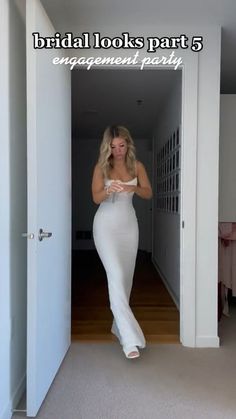 a woman in a white dress is walking through an open door and looking at the camera