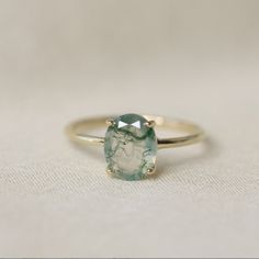 a ring with a green stone on it sitting on a tableclothed surface in front of a white background