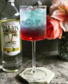 a close up of a drink in a glass near a bottle on a table with flowers