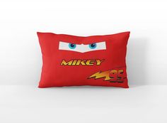 a red pillow with the face of mikey from cars printed on it, sitting against a white wall