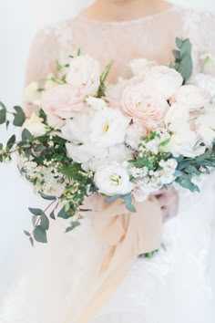 a bride holding a bouquet of white and pink flowers with greenery in her hands