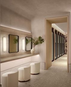 an empty hallway with white stools and mirrors on the wall, along with potted plants