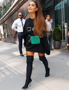 a woman wearing thigh high boots and a black sweater is seen walking down the street