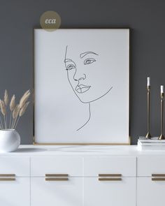 a white cabinet with a black and white drawing on the wall next to a vase filled with dry grass