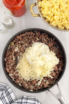 pasta, meat and cheese in a skillet on a counter with utensils