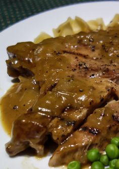 a white plate topped with pasta and meat covered in gravy next to peas