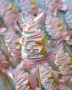 pink and blue cupcakes with gold leaf decorations on them are arranged in rows