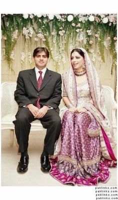 a man and woman sitting next to each other in front of a flower covered wall