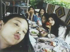 a group of young women sitting around a table eating food and drinking tea or coffee